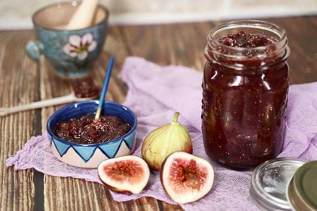 A jar and bowl of fig jam with some fresh figs beside, over a table