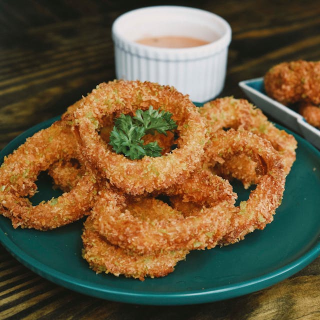 A plate of crispy golden fried calamari rings, with a small bowl of sauce.